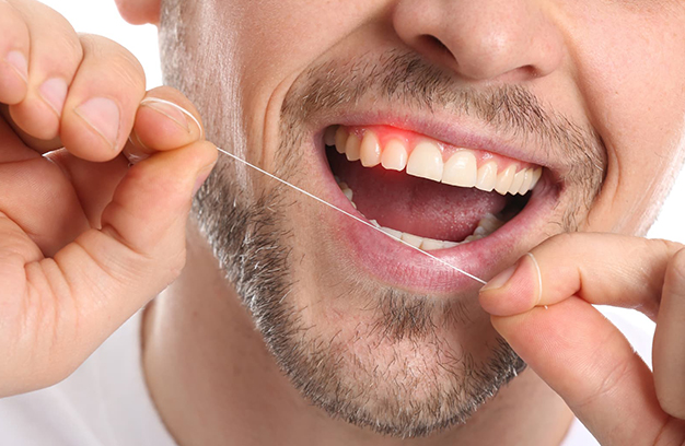 Man flossing teeth with dental floss, demonstrating proper oral hygiene practice.