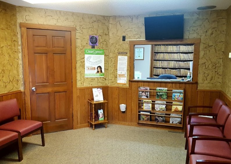 Dental office waiting room with seating, magazines, and informational materials on walls.